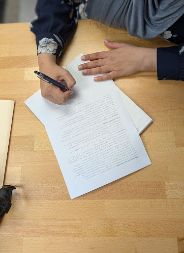 Corporate bookkeeper from A.M.I. CPA Professional Corporation, doing paperwork for a client at a table.