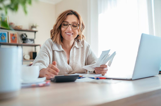 Woman sitting at a desk in her home using a calculator to prepare her taxes.