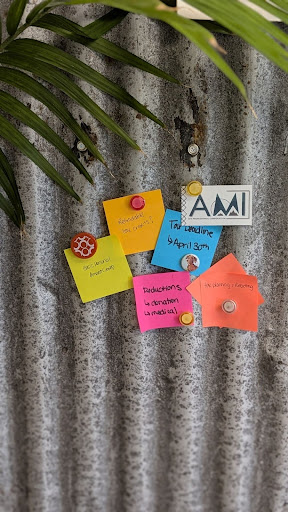 Metal wall with greenery in the top left corner and various colours of sticky notes with tax reminders and a business card from AMI CPA Professional Corporation pinned up with magnets.