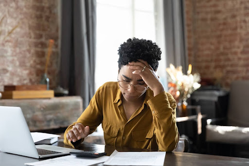 Unhappy woman sitting at a desk with a calculator going over bookkeeping mistakes for her business.